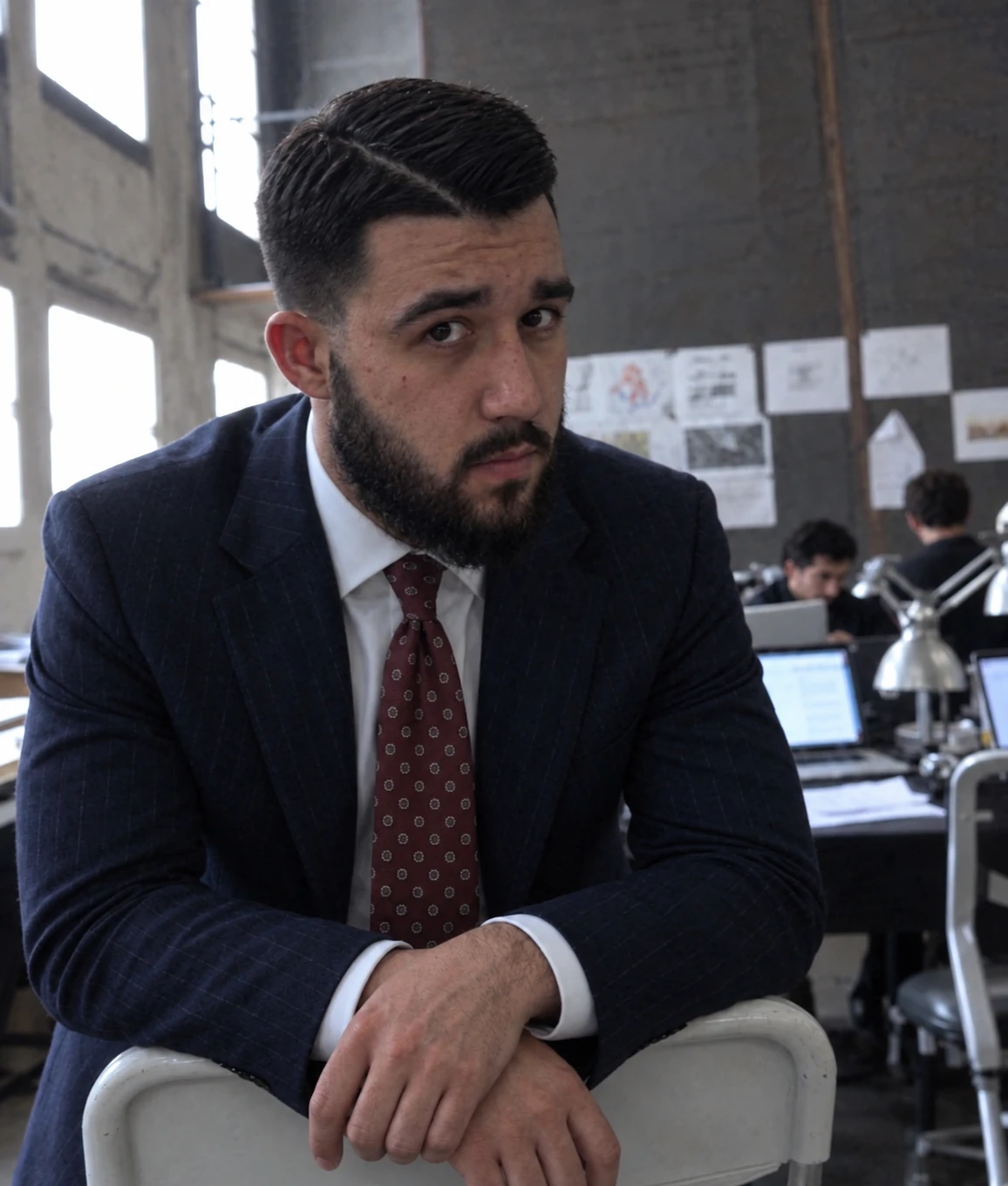 Abdurauf, the founder, in a navy pinstripe suit and tie, leaning on the back of a chair in the studio.
