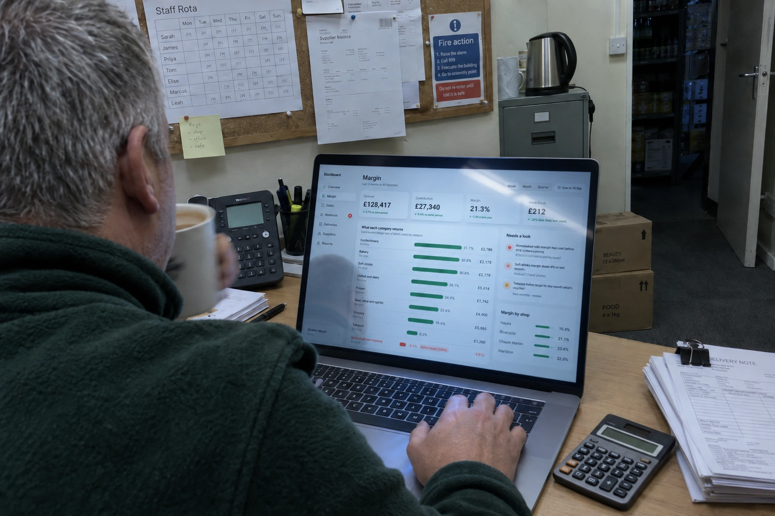 The shop owner at a desk in the back office, mug in hand, reading the week's margin report on a laptop.